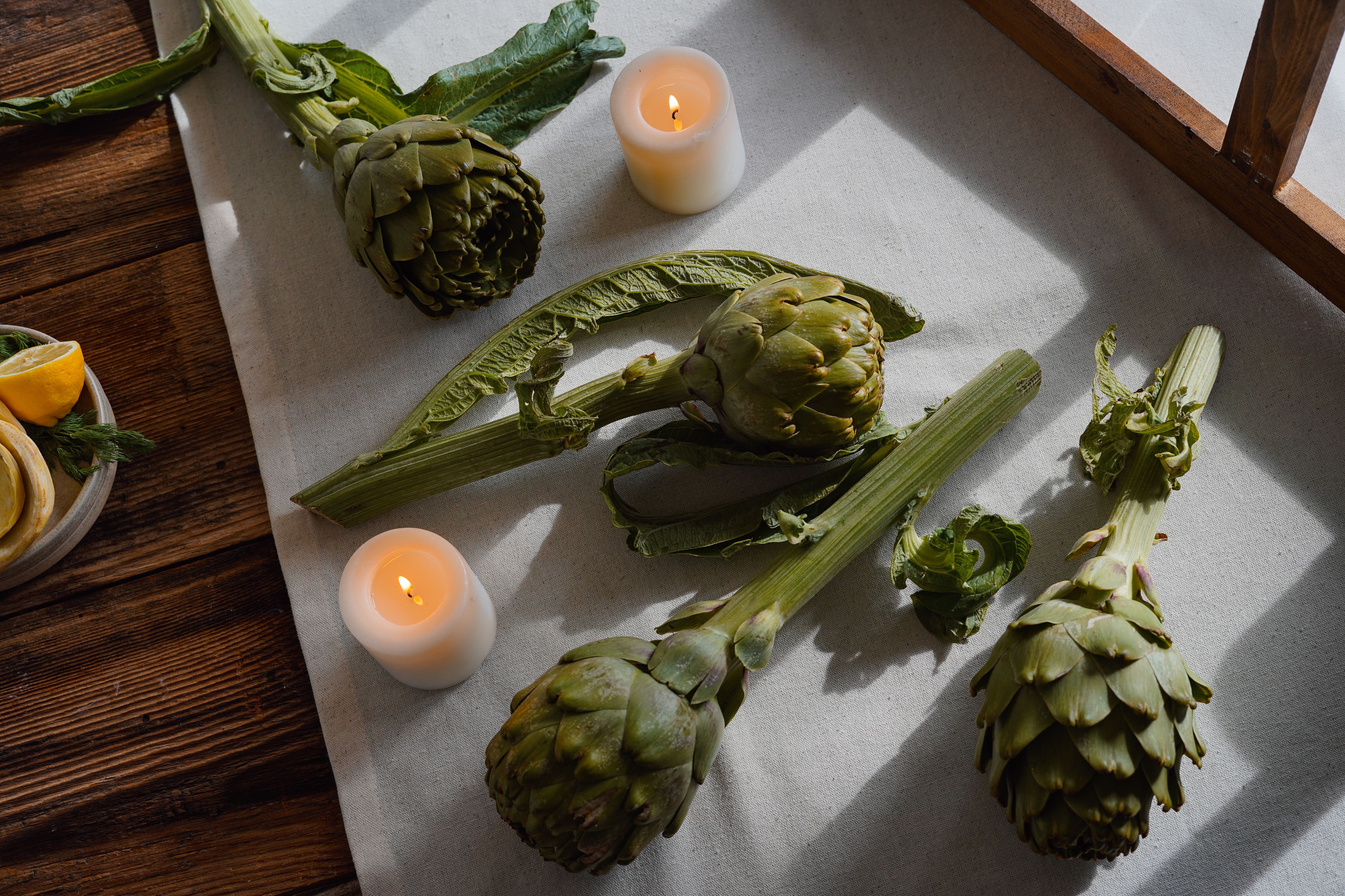 A cozy still life of fresh artichokes and candles on a rustic wooden table.