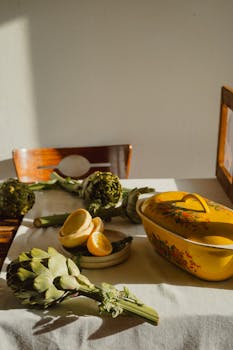 A charming rustic table with fresh artichokes, sliced lemons, and a floral yellow casserole dish.