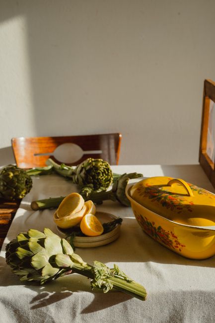 A charming rustic table with fresh artichokes, sliced lemons, and a floral yellow casserole dish.