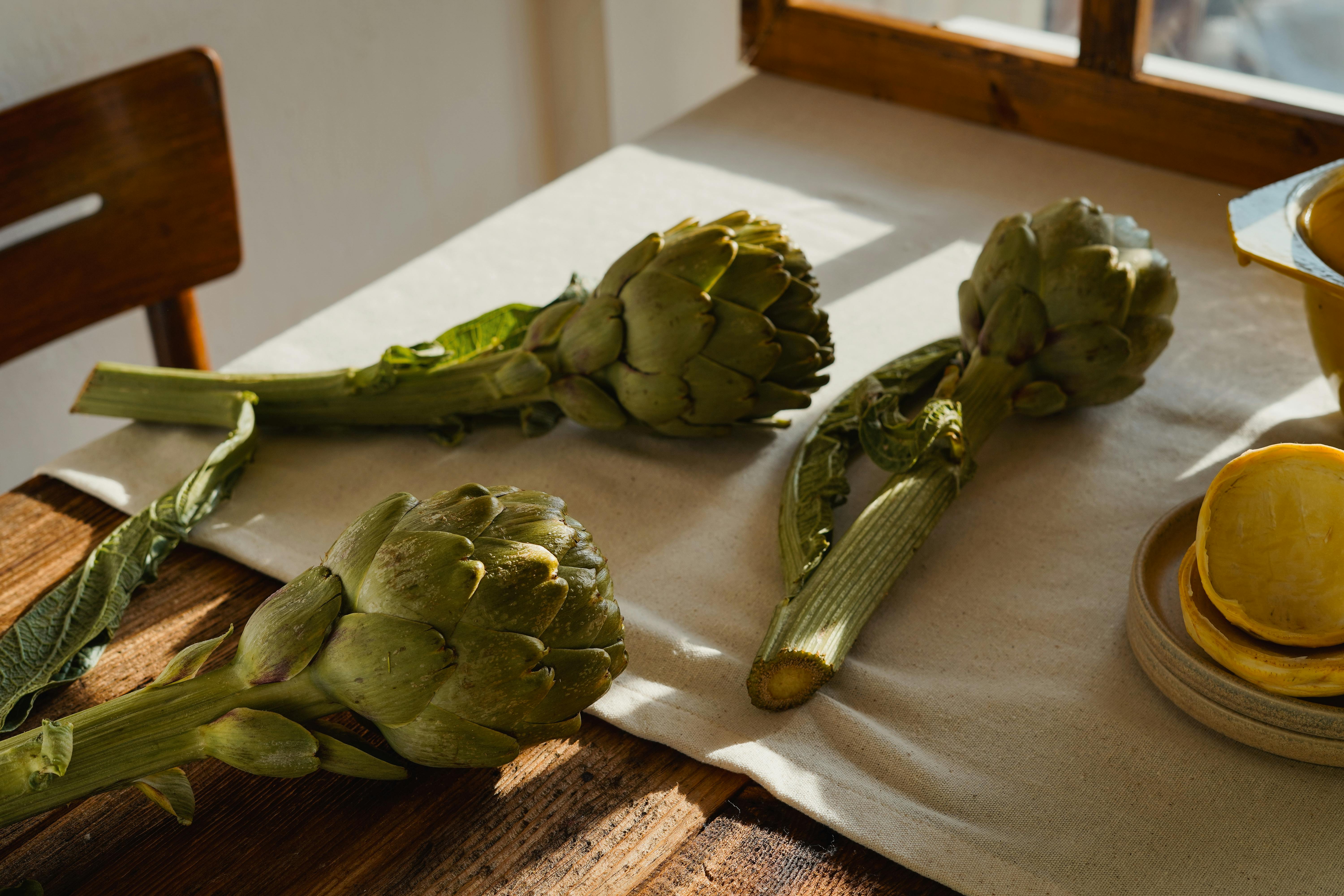 Whole Artichokes And Artichoke Hearts On A Wooden Table