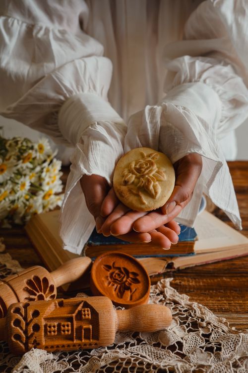 Free Hands holding a decorative cookie with wooden molds on a rustic table, evoking a traditional baking theme. Stock Photo