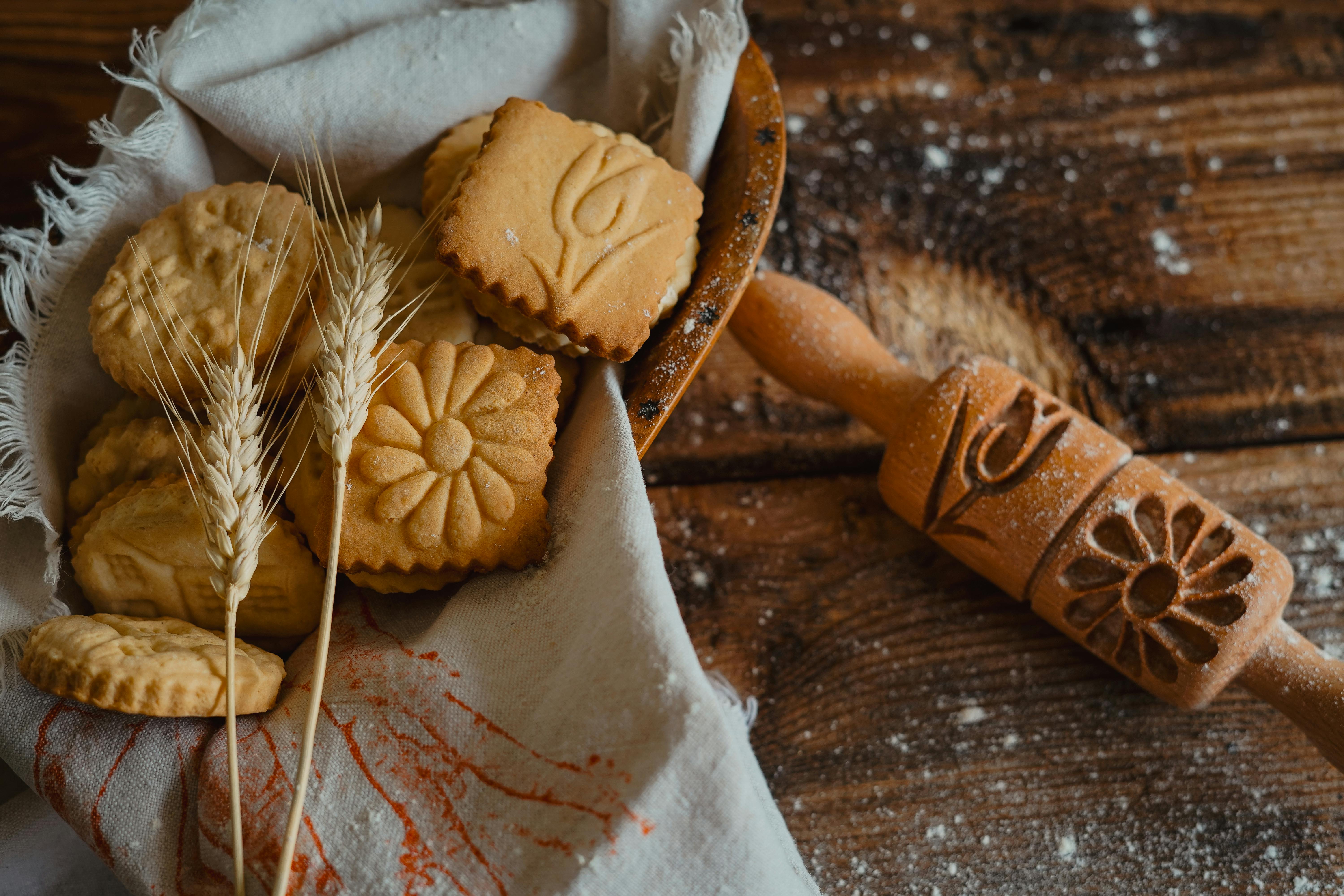 Artisan cookies with embossed designs next to a decorative rolling pin on rustic wooden surface.