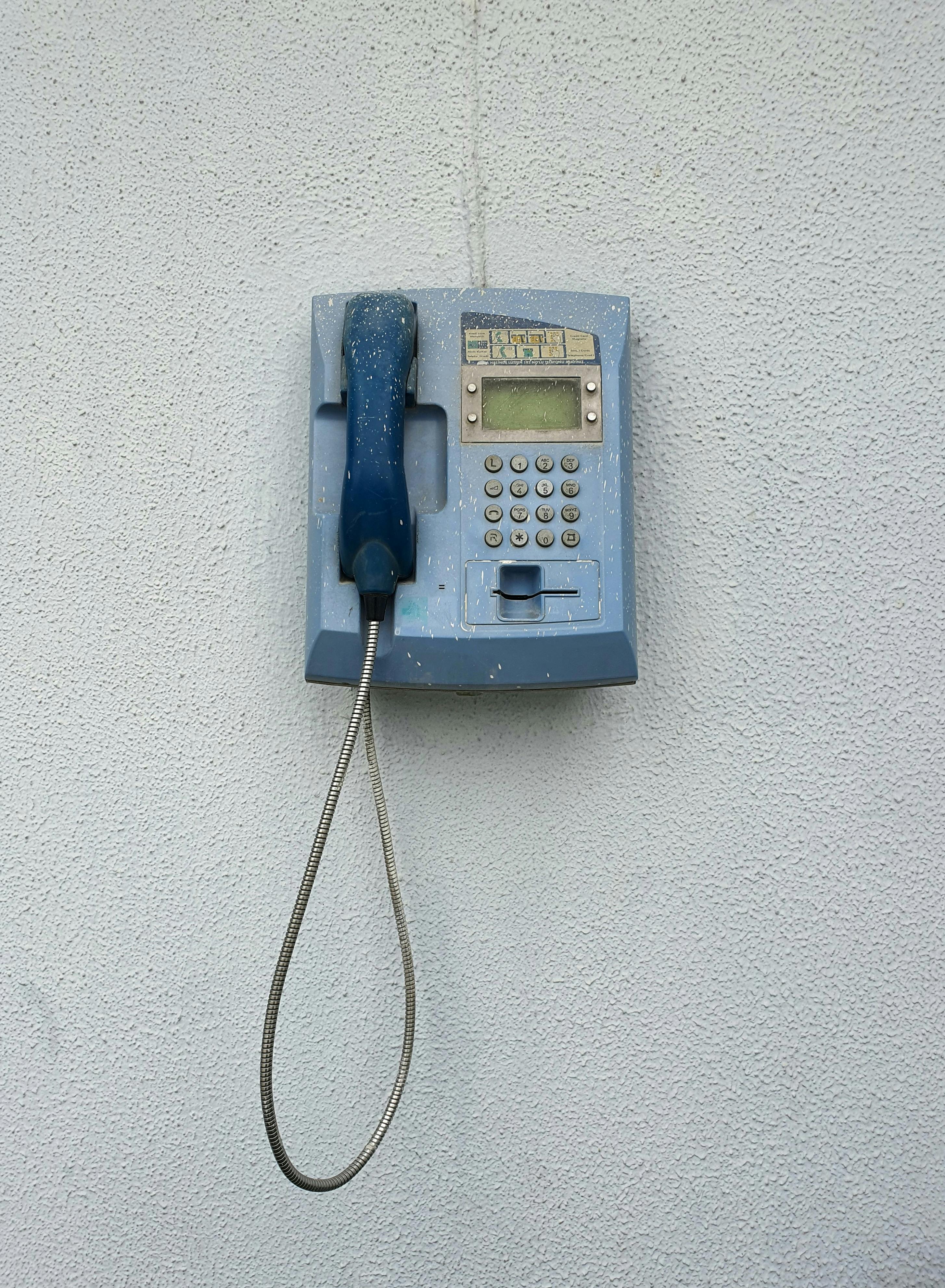 Zadarmo Oldschoolový modrý telefónny automat namontovaný na bielej štruktúrovanej stene, vintage retro vzhľad. Fotka z fotobanky