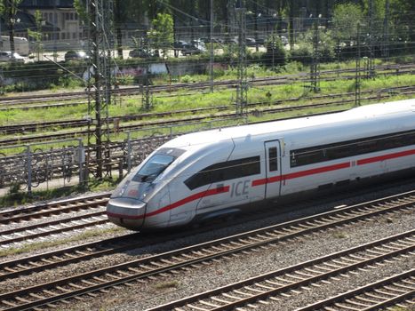 An ICE train speeding down the tracks on a sunny day with greenery in the background.