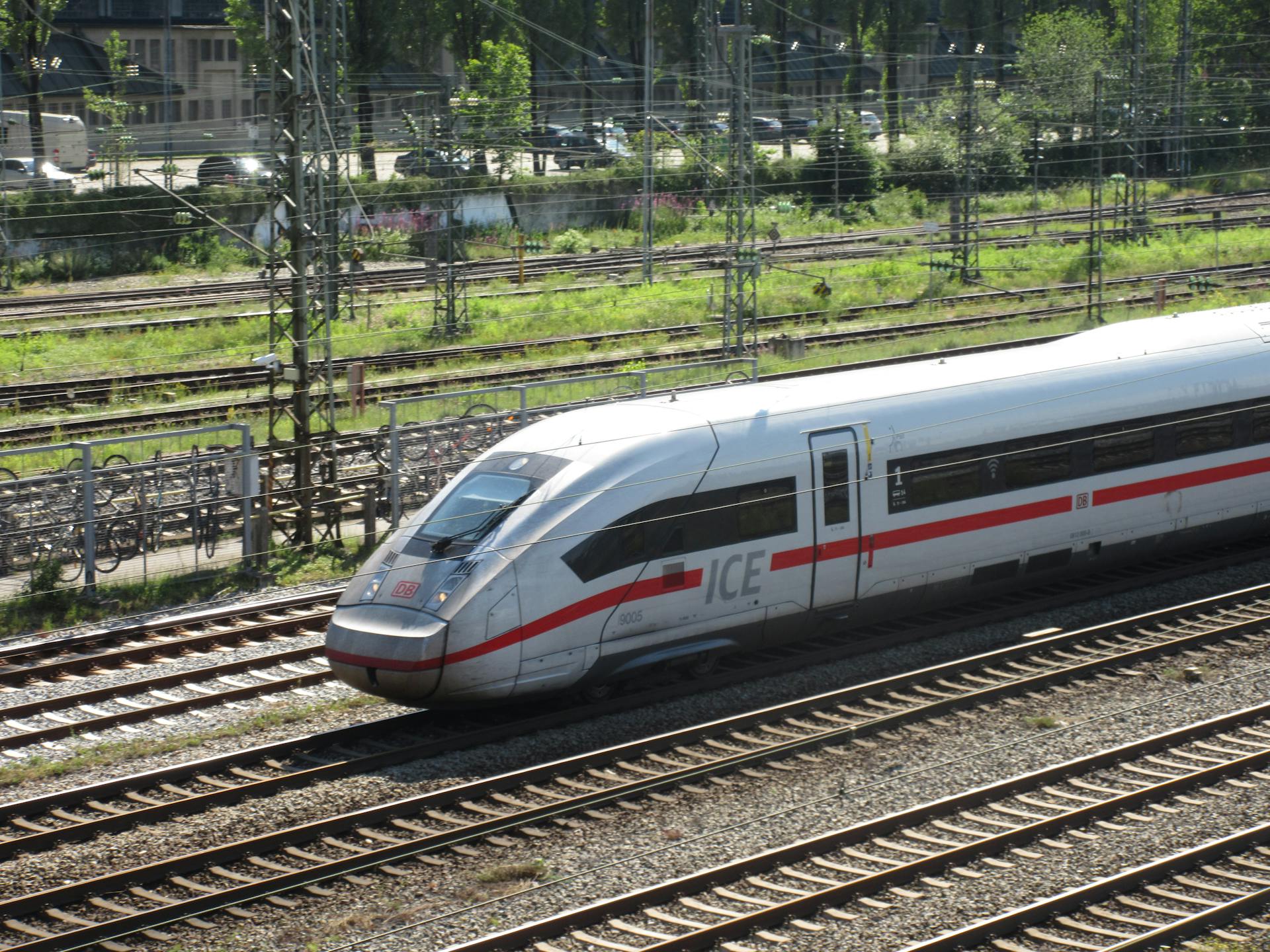 An ICE train speeding down the tracks on a sunny day with greenery in the background.