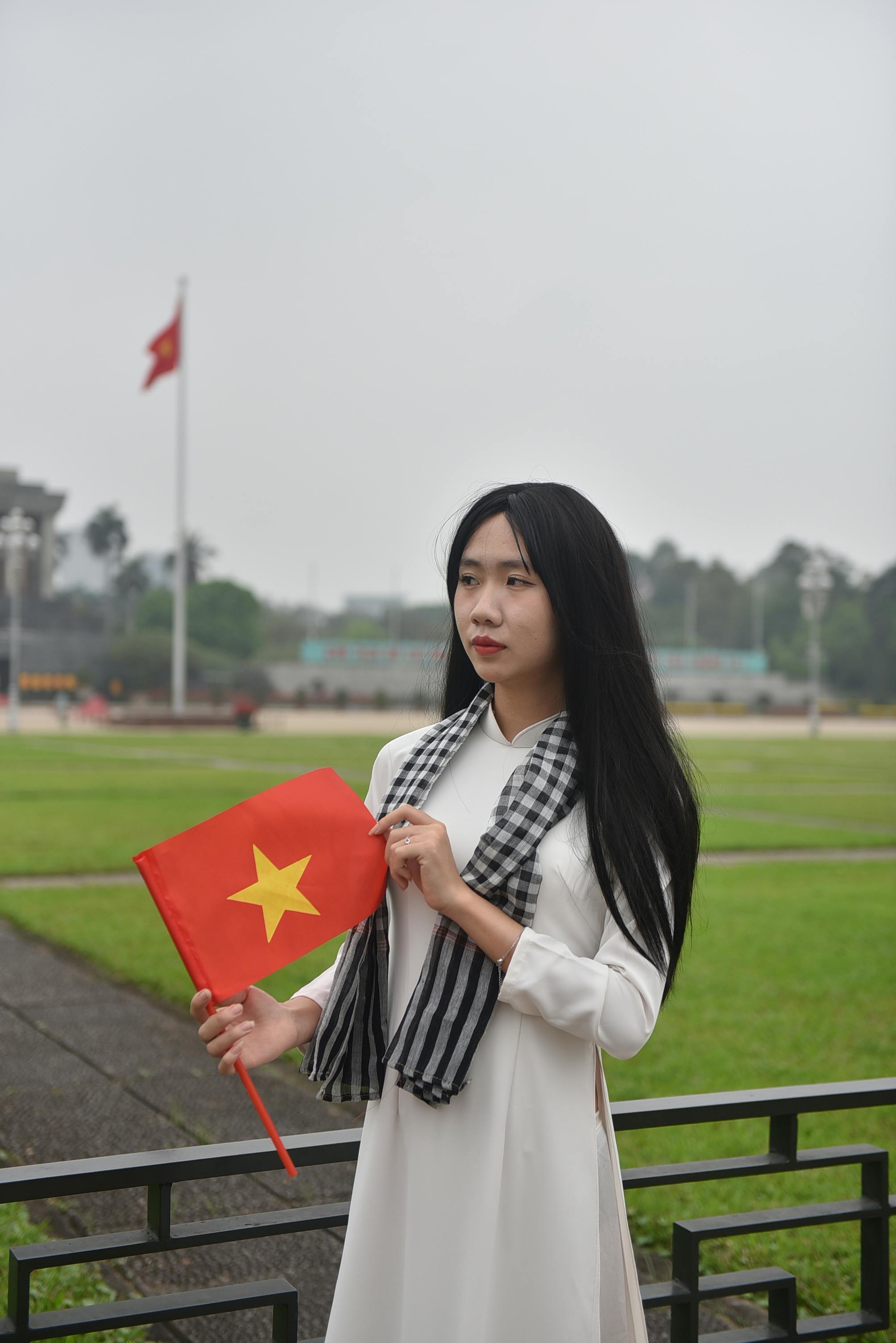 Vietnamese woman in traditional dress holds flag at recognizable landmark, showcasing cultural pride.