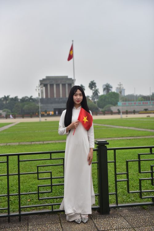 Free A woman in traditional attire holding the Vietnam flag at Ho Chi Minh Mausoleum, Hanoi. Stock Photo