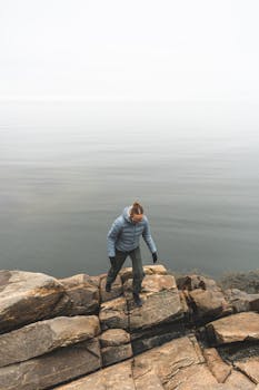 A lone hiker navigates a rocky shoreline against a serene sea backdrop.