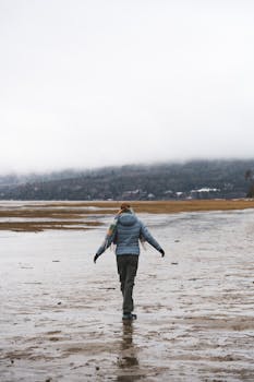 A person strolls alone on a scenic, misty beach with distant mountains.