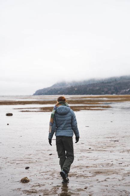 A lone woman walks on a misty, serene beach with distant mountains.