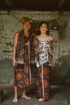A couple in traditional Balinese clothing standing indoors, showcasing cultural heritage.
