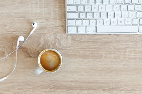 Free Beverage Filled Mug Near Apple Airpods With Lightning Connector and Apple Magic Keyboard Stock Photo
