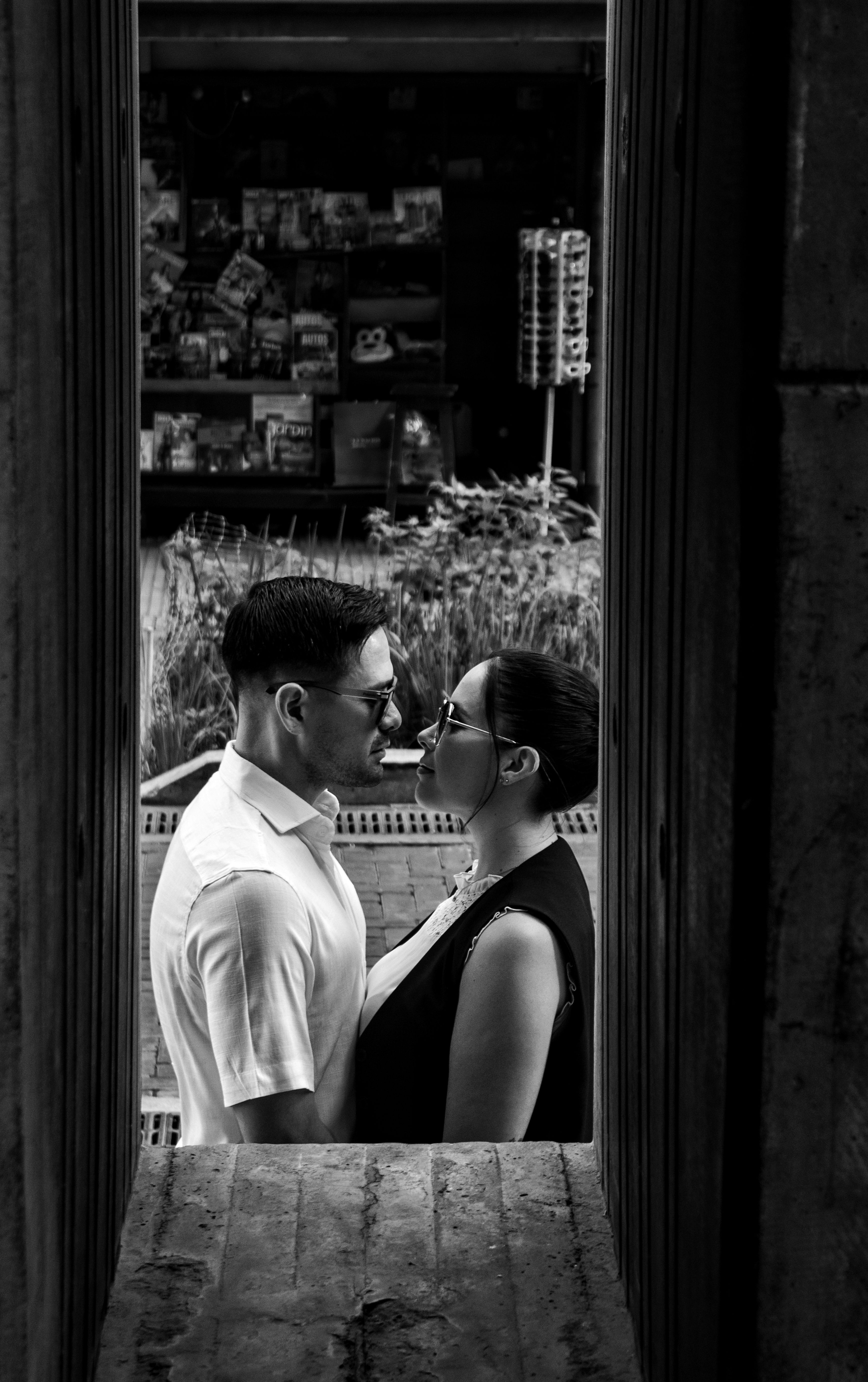 A loving couple stands close embracing in a stylish urban setting, captured in black and white.