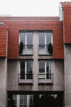 A contemporary residential building featuring a unique red tiled roof and symmetrical design in an urban setting.