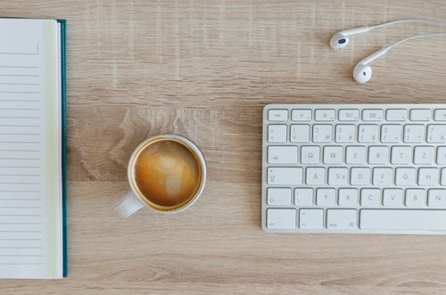Free A tidy workspace with a notebook, coffee cup, keyboard, and earphones on a wooden desk. Stock Photo