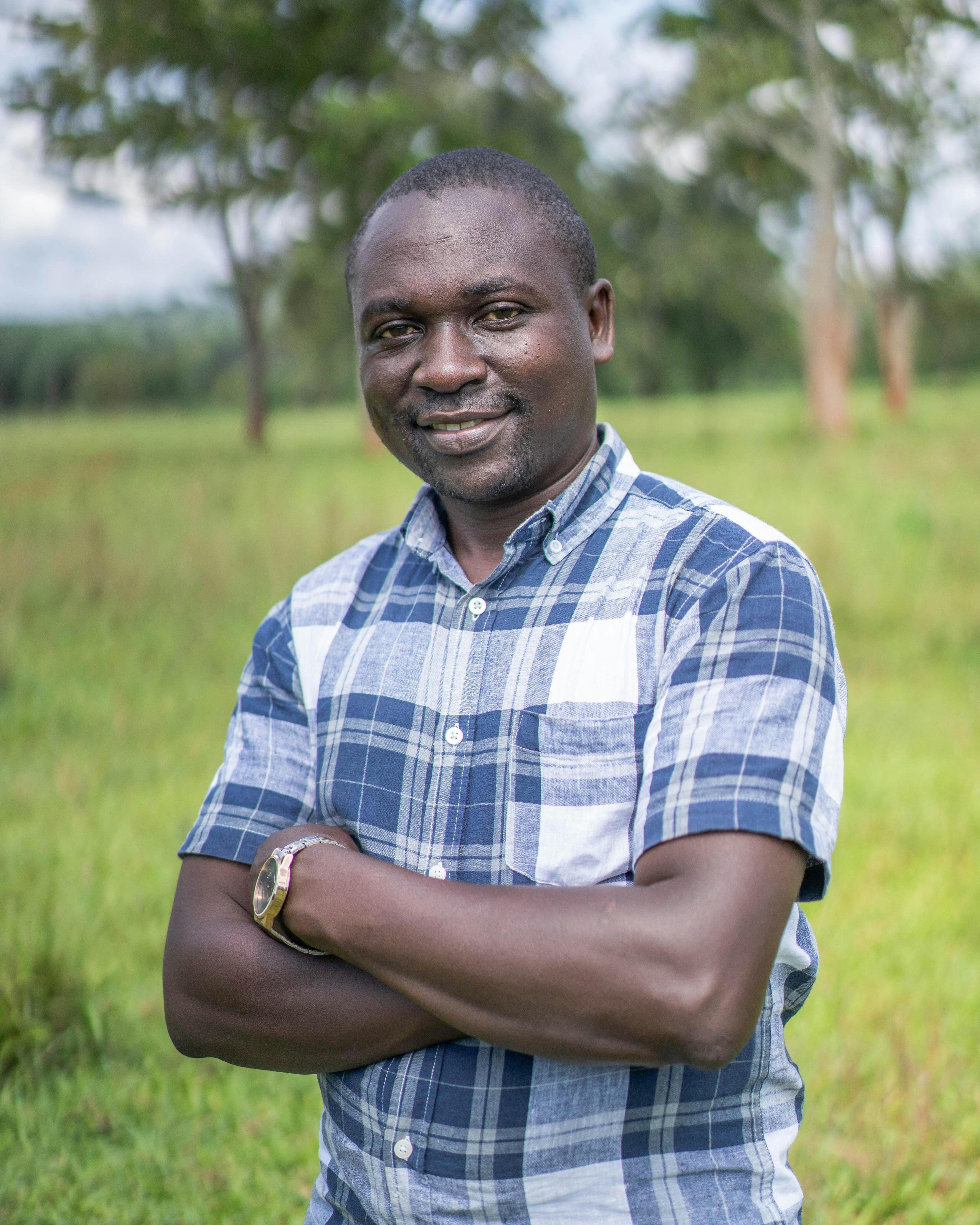 Smiling man crossing arms in a field, exuding confidence and positivity.