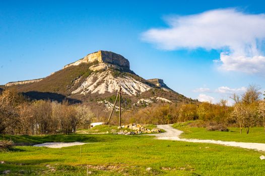 A captivating view of a lone mountain surrounded by lush spring vegetation under a blue sky.