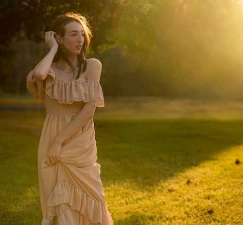 Free A woman in a beige dress stands gracefully in a sunlit meadow during golden hour. Stock Photo