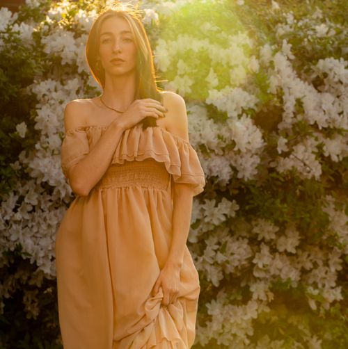 Free Elegant woman in flowing dress posing gracefully in a sunlit garden, exuding warmth and beauty. Stock Photo