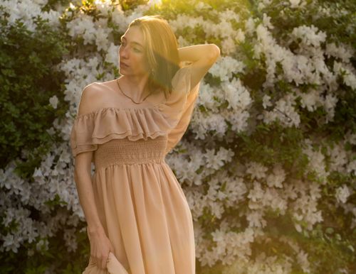 Free Graceful woman in a light dress posing in a sunlit garden with white flowers. Stock Photo