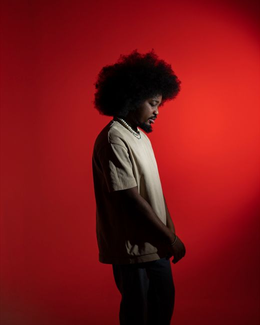 A striking side-profile portrait of a person against a vivid red background.