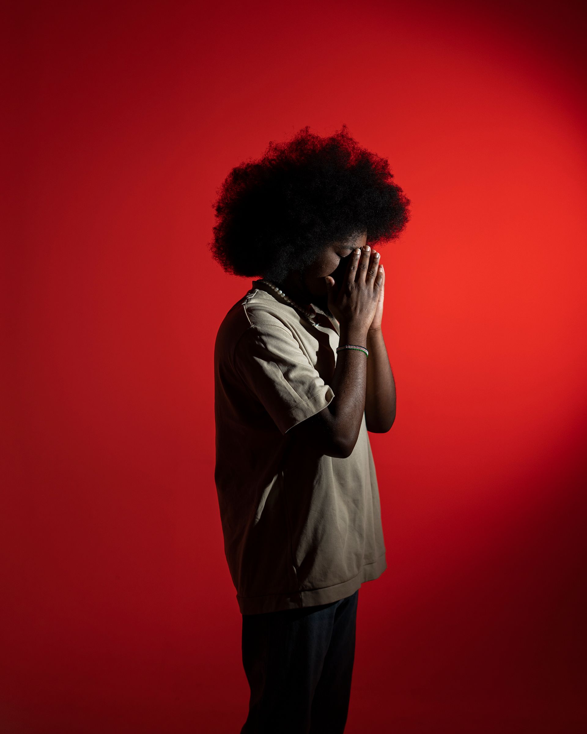 Profile of man praying with closed eyes against a vibrant red background, creating a dramatic and introspective mood.