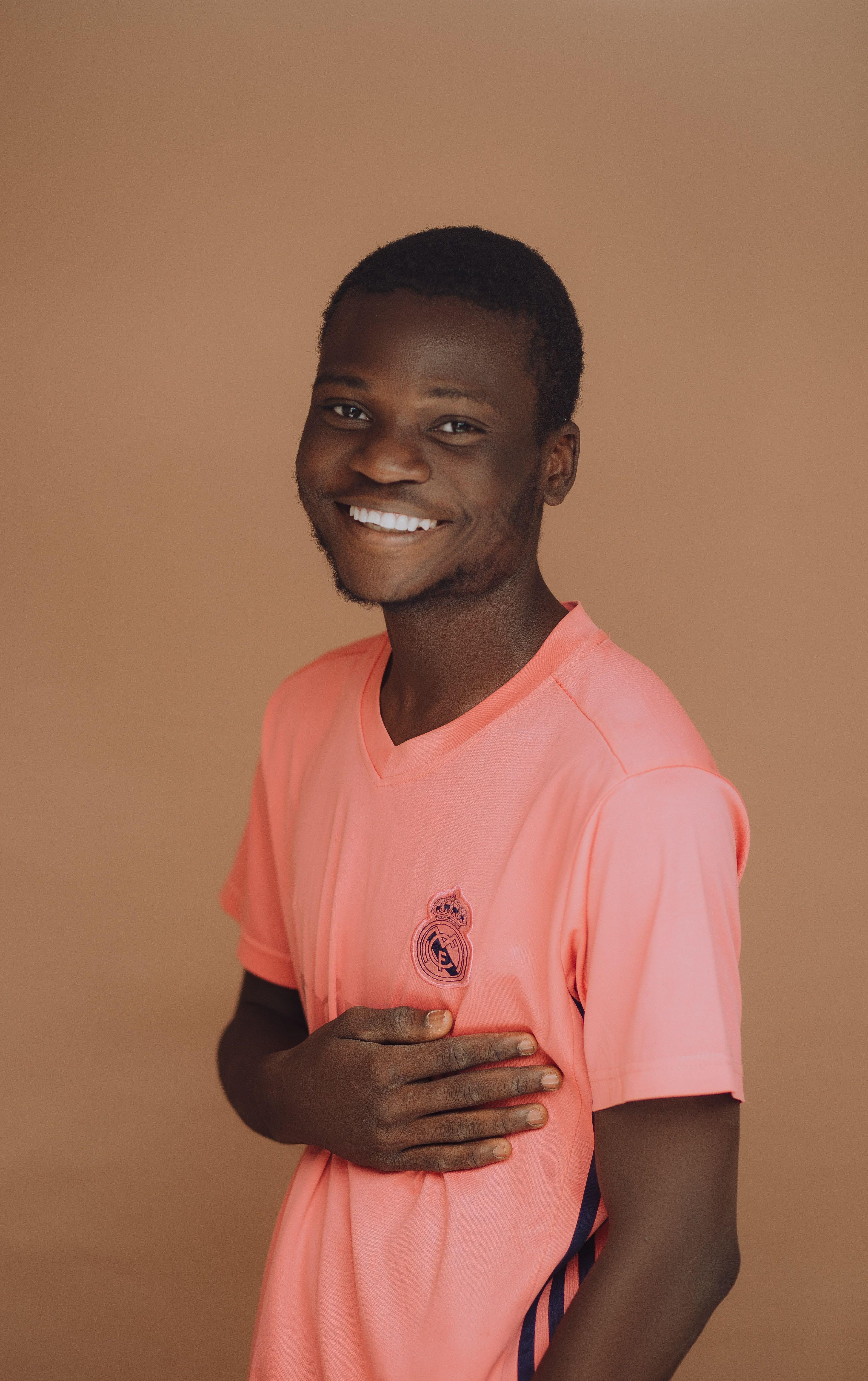 Portrait of a smiling young man wearing a pink t-shirt against a brown background.