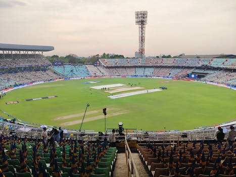 Wide-angle view of an iconic cricket stadium empty before a match, showcasing vibrant seating and green pitch.