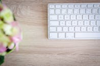 从顶视图看，干净的工作空间里，木桌上摆着白色键盘和模糊的花朵