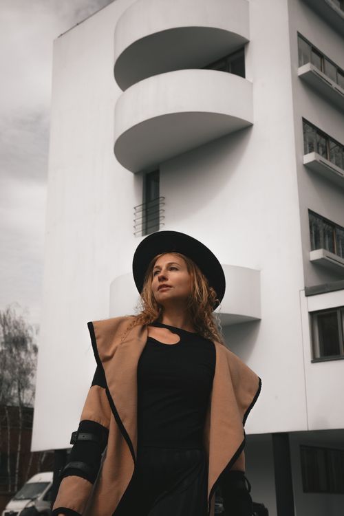 Free Fashionable woman in a hat standing in front of a modern white building. Stock Photo