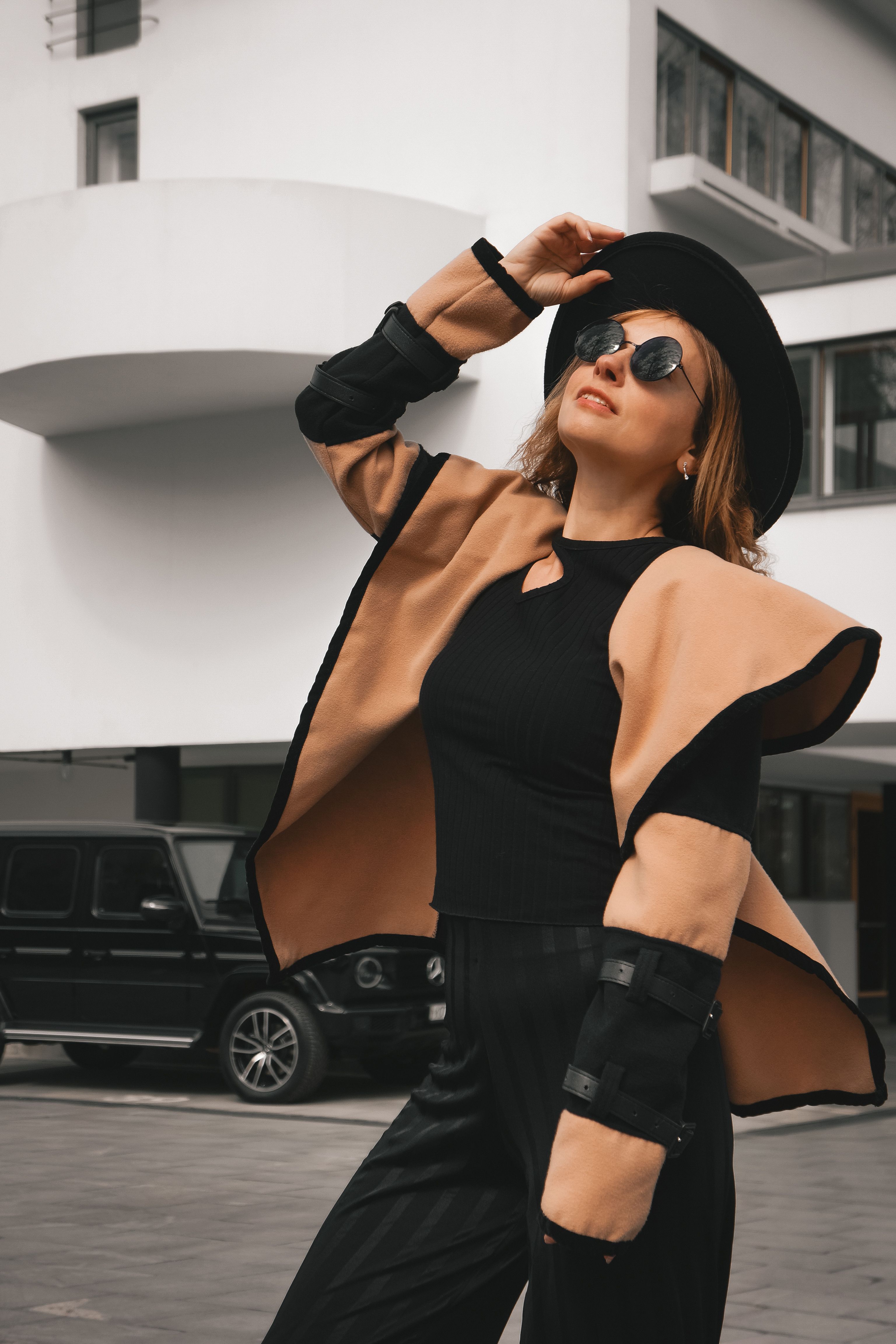 Fashionable woman in modern clothing and sunglasses striking a pose outside an urban setting.