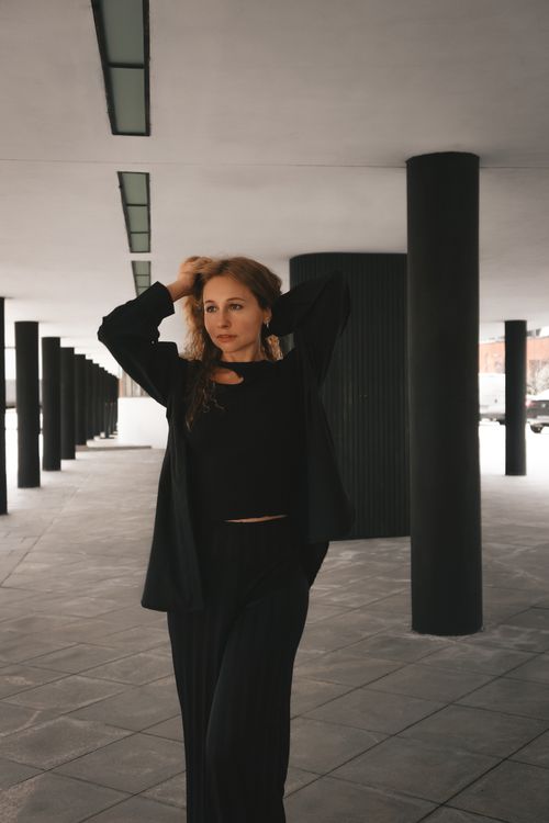 Free Stylish woman in black outfit poses confidently in urban architecture setting. Stock Photo