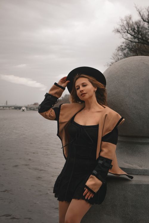 Free Elegant woman in fall fashion leans on a stone railing by a serene riverside. Stock Photo