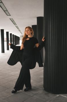 Stylish woman in black outfit posing confidently in a modern architectural space.