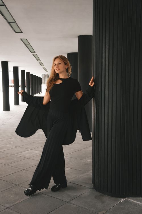 Free Stylish woman in black outfit posing confidently in a modern architectural space. Stock Photo