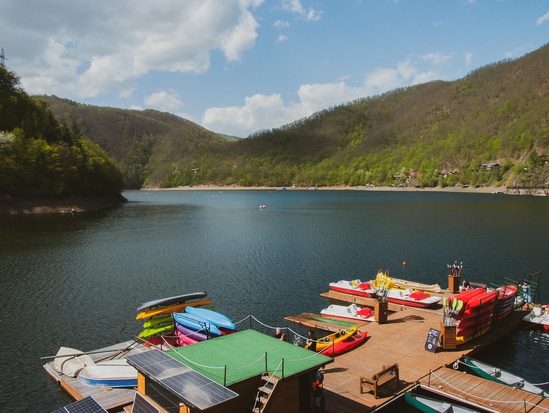 A serene lake view with vibrant kayaks on a wooden dock surrounded by lush green hills.