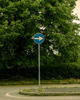 A serene street scene with a directional sign amidst lush greenery in Milan, Italy.