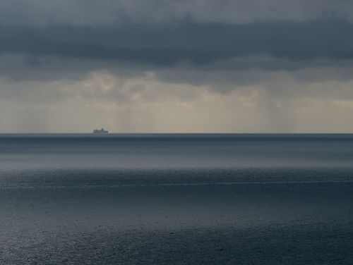 Free A lone ship sails under stormy clouds on a vast and moody sea horizon. Stock Photo
