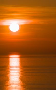 Captivating sunrise over calm sea with vibrant orange hues and reflected sunlight on water.