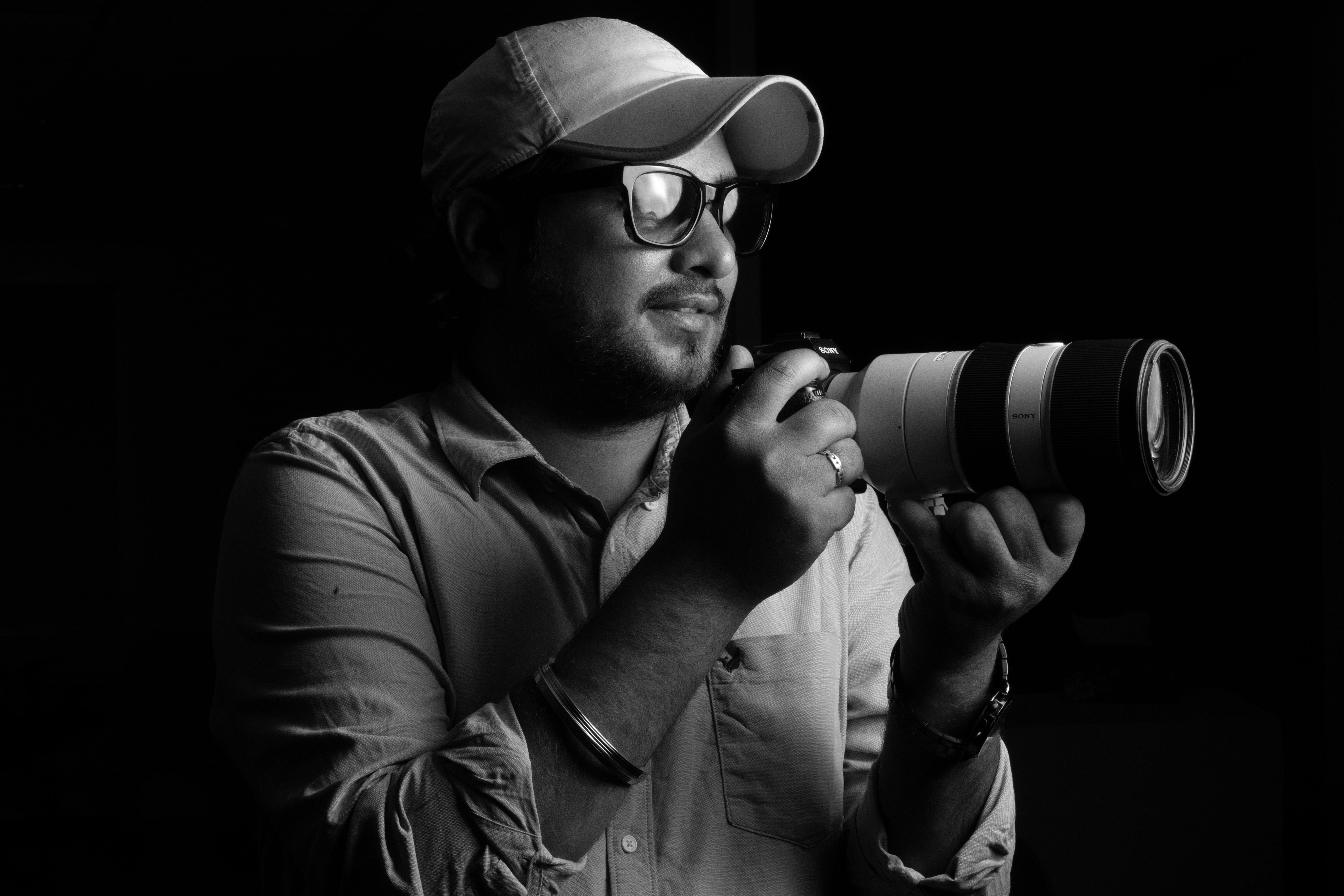 Black and white portrait of a male photographer holding a camera with a long lens.