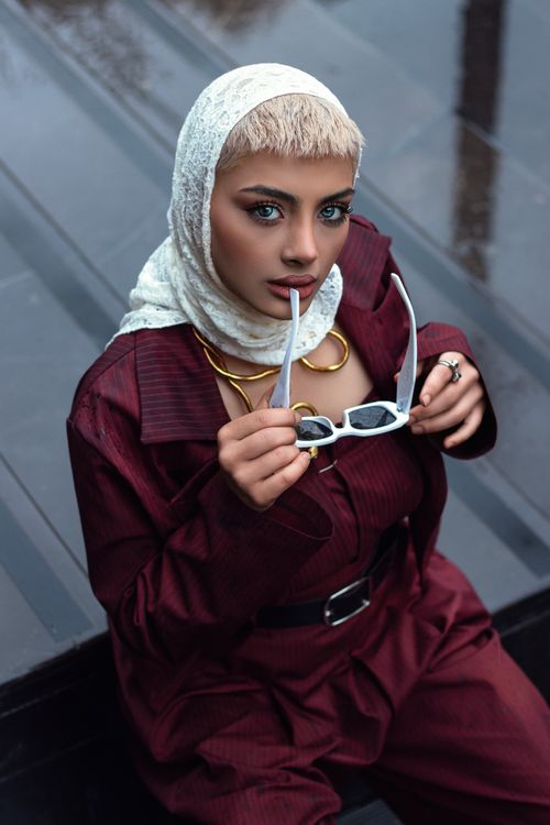 Free Portrait of a fashionable woman in a burgundy outfit and hijab holding sunglasses. Stock Photo
