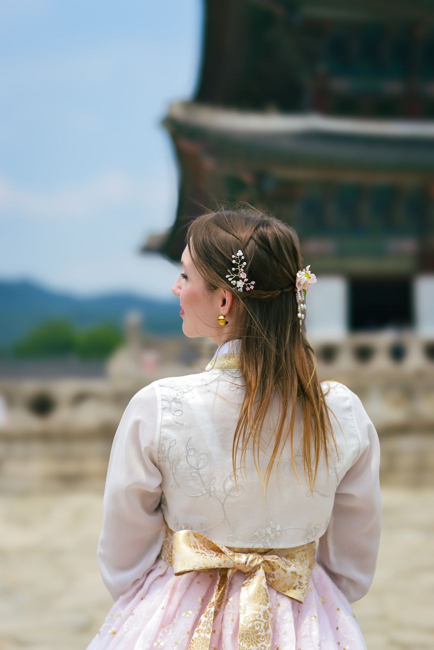Une femme portant un hanbok admire l'architecture ancienne d'un palais en Corée du Sud.