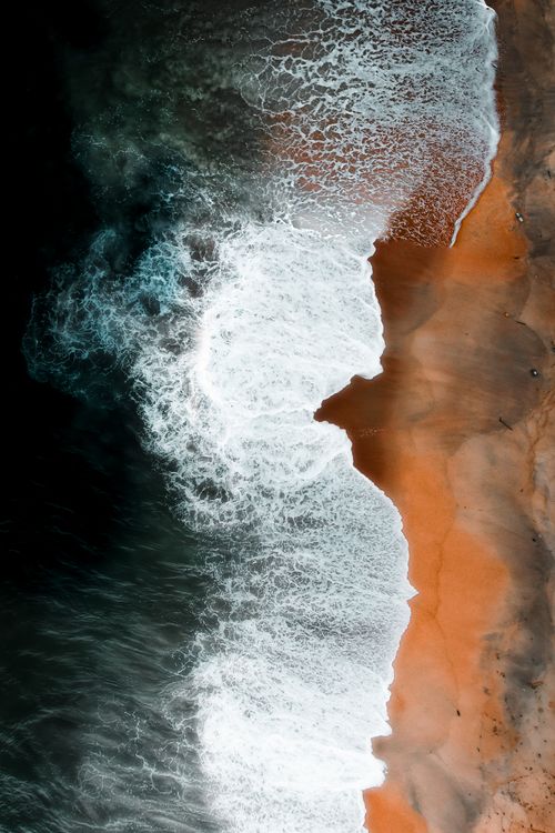 Free Stunning aerial shot showcasing ocean waves crashing onto a sandy shore with vibrant contrast. Stock Photo