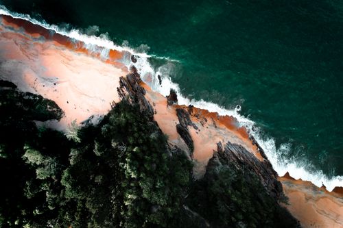 Free Breathtaking aerial view of a vibrant coastline with lush greenery and crashing waves on rocky shores. Stock Photo