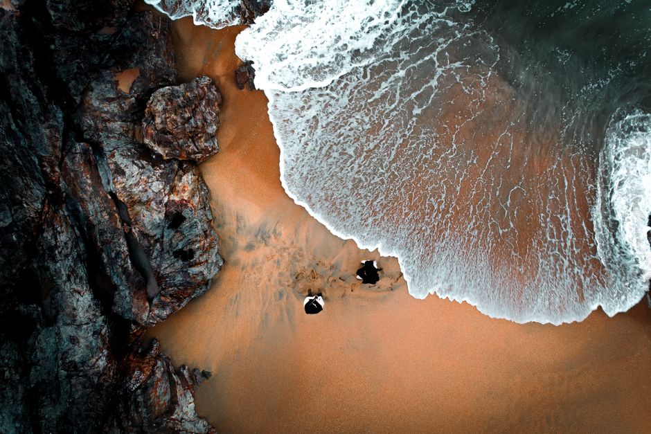A stunning aerial view of waves crashing on a sandy beach with surrounding rocks.