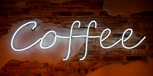 Free Glowing white neon coffee sign on rustic brick wall in cafe interior. Stock Photo