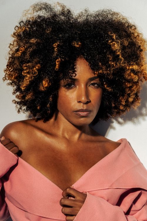 Free Stunning portrait of a woman with voluminous curly hair in a pink top. Stock Photo