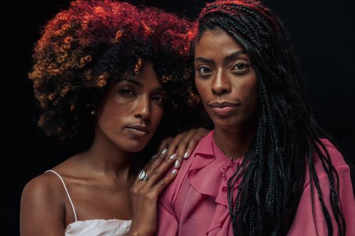 Free Close-up portrait of two women embracing with unique hairstyles on a black background. Stock Photo