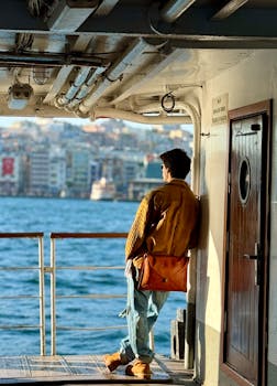 Man standing on a ferry in Istanbul, gazing at the cityscape across the Bosphorus.