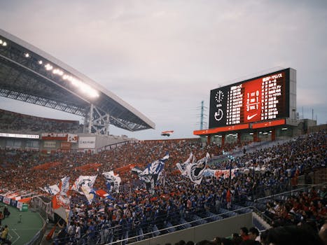 A lively soccer stadium scene with fans waving flags and a scoreboard displaying match details.